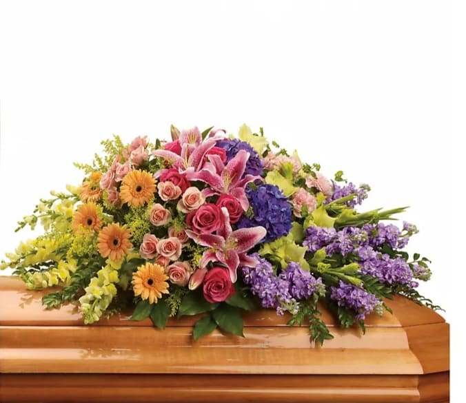 Colorful floral casket spray with pink lilies, roses, and purple blooms