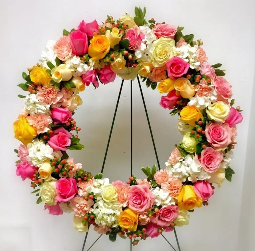 Circular floral wreath with pink, yellow, and white roses on a stand