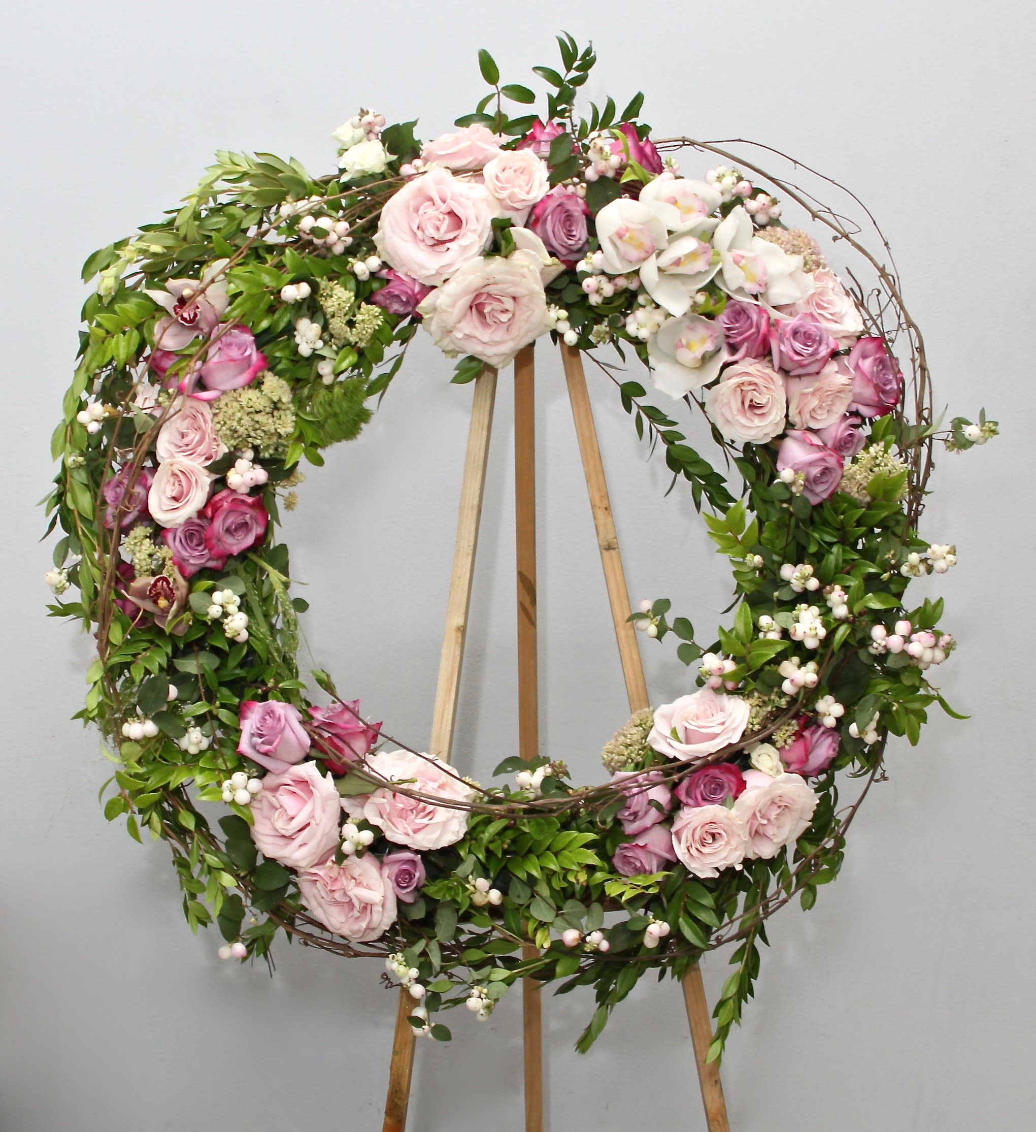 Circular floral wreath with pink and white roses on a wooden stand