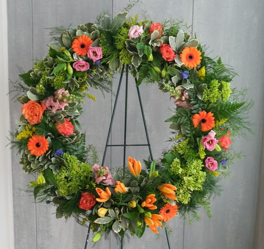 Large floral wreath with orange, pink, and green flowers on a black stand