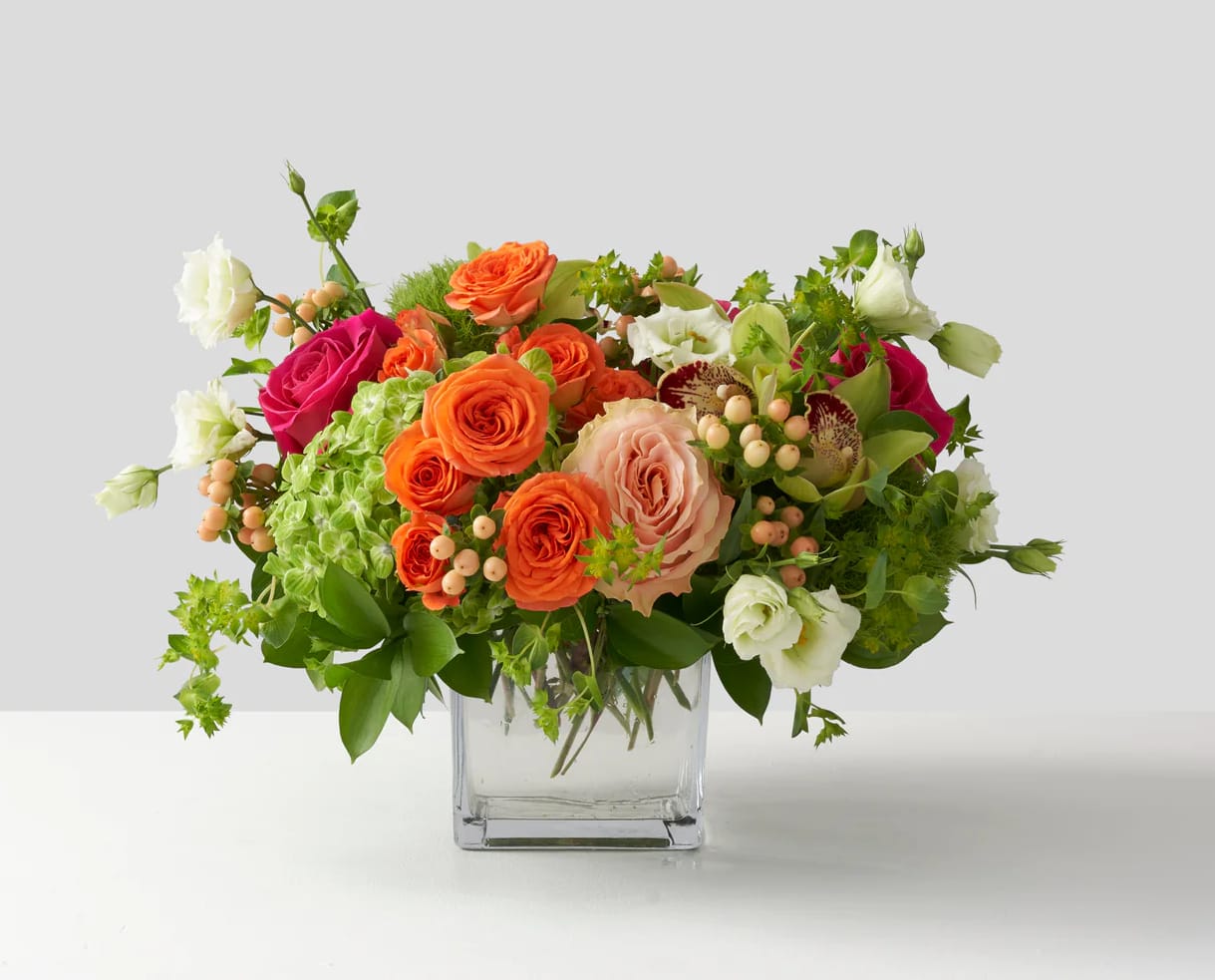 Mixed bouquet of orange, pink, and white roses in a clear glass vase