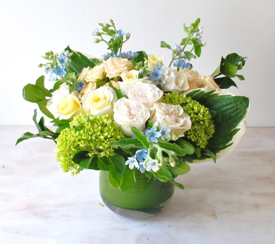 Bouquet of cream roses and blue flowers in a green glass vase