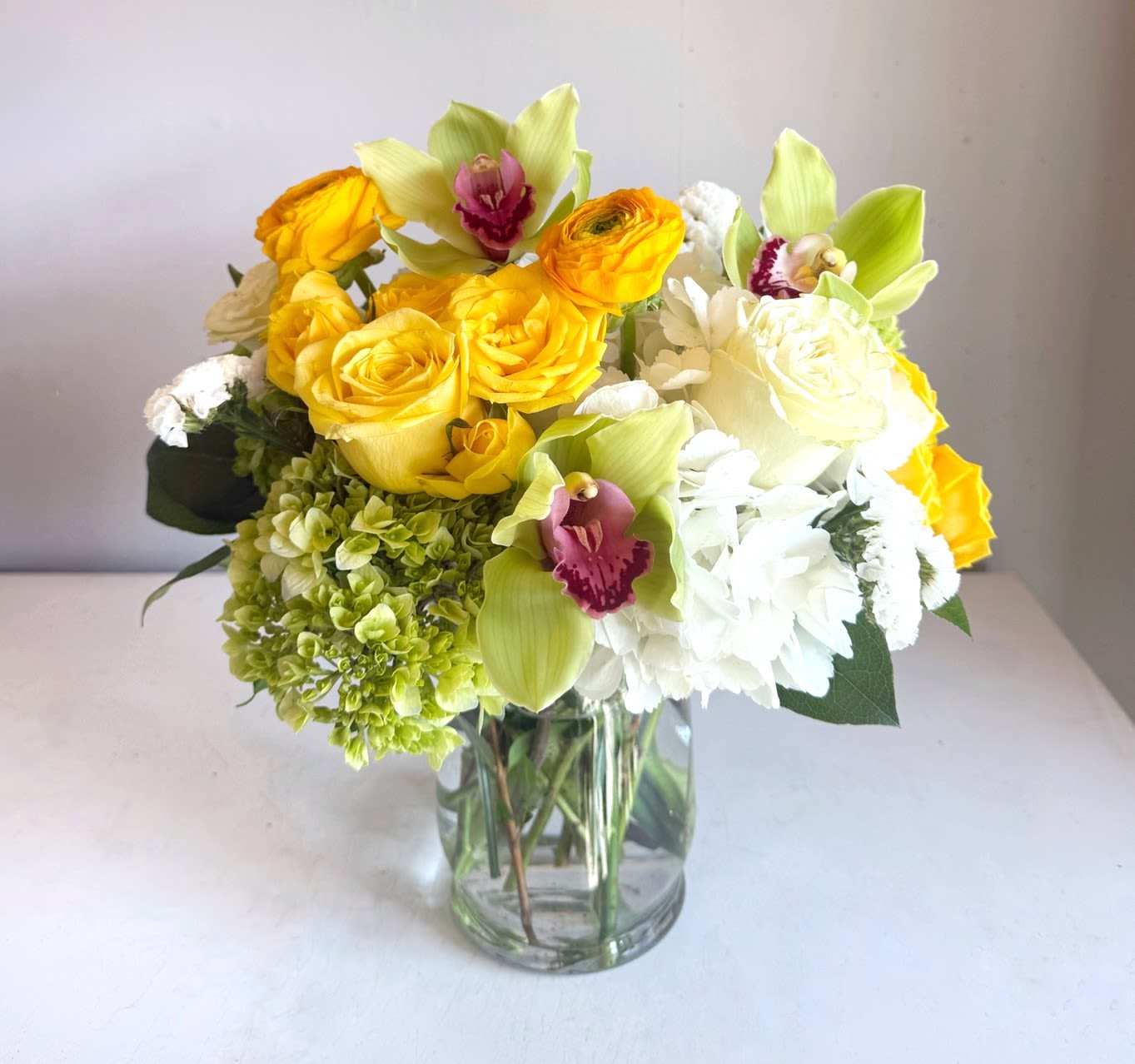 Yellow roses and white flowers in a clear glass vase