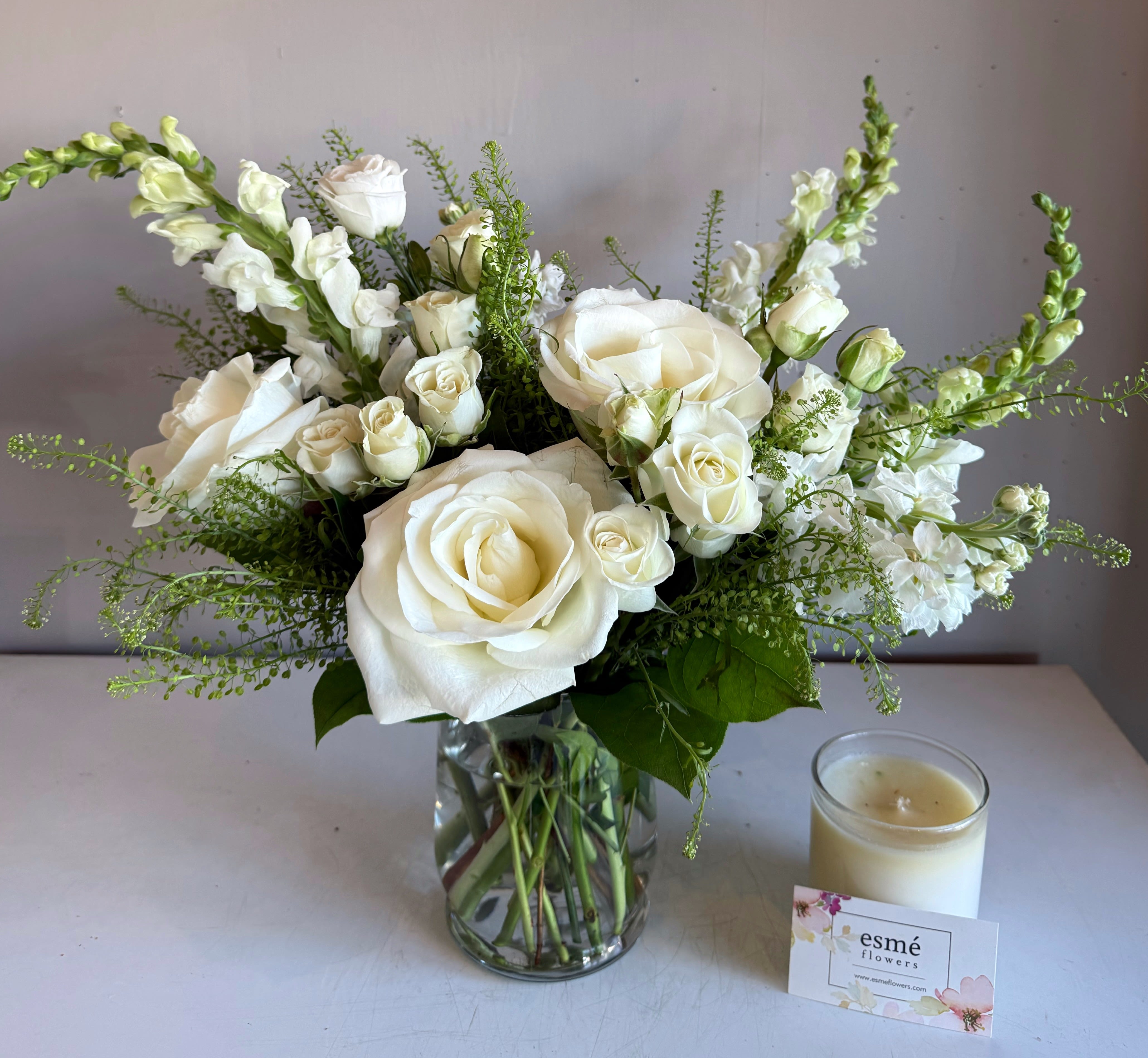 White roses and snapdragons in a glass vase beside a candle
