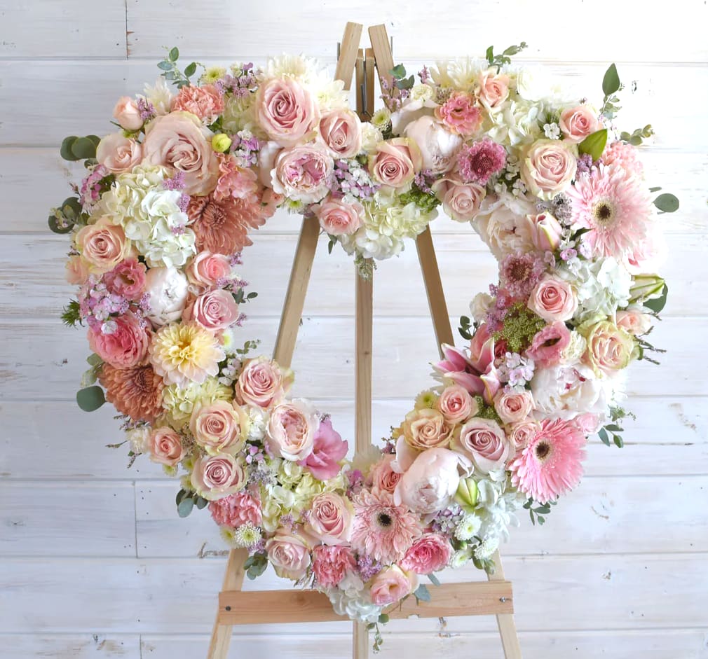 Heart-shaped floral wreath on a wooden easel with pink and white flowers