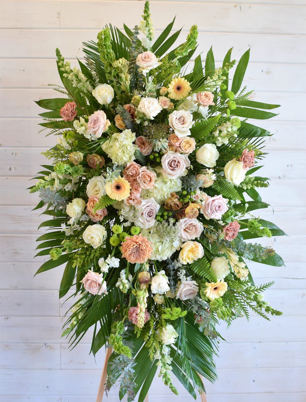 Large standing spray of pastel roses and mixed flowers with tropical greenery