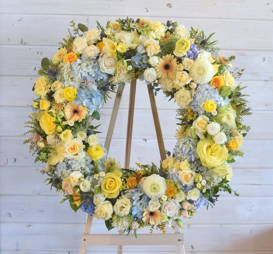Large floral wreath of yellow, white, and blue flowers on a wooden stand