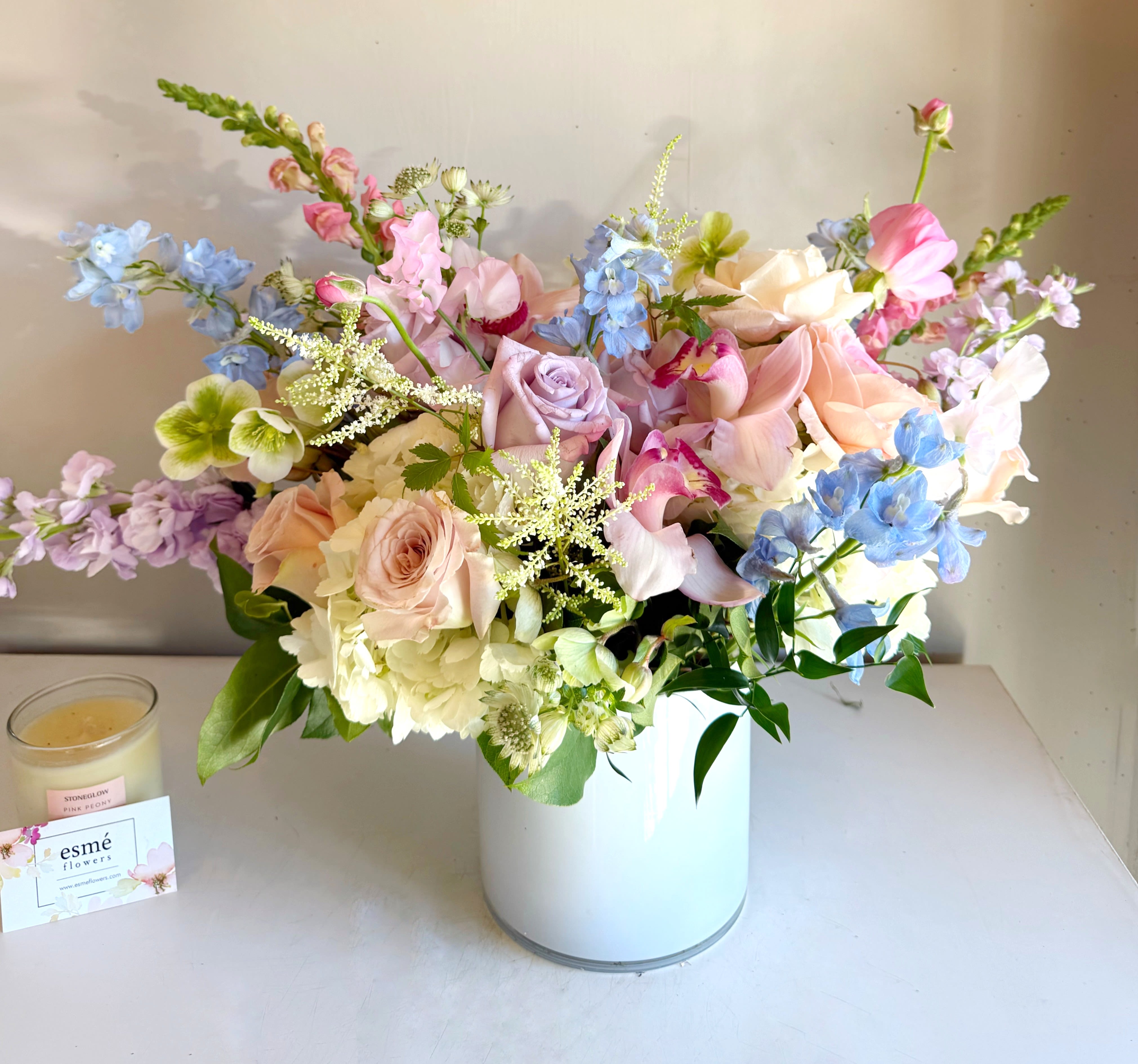 Morning Mist - Light and airy, whimsical yet elegant,  Morning Sky features New Zealand cymbidium orchids, soft blue delphiniums, ocean song, and seasonal pastel blooms in a white vase.