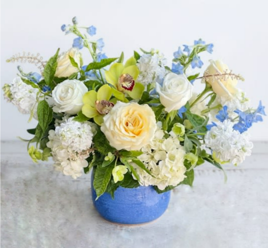 Mira - Soft and elegant with a pop of cymbidium greens, Mira is a gorgeos arrangement featuring playa blanca roses, New Zealand cymbidium orchids, soft blue delphiniums, hydrangeas. 