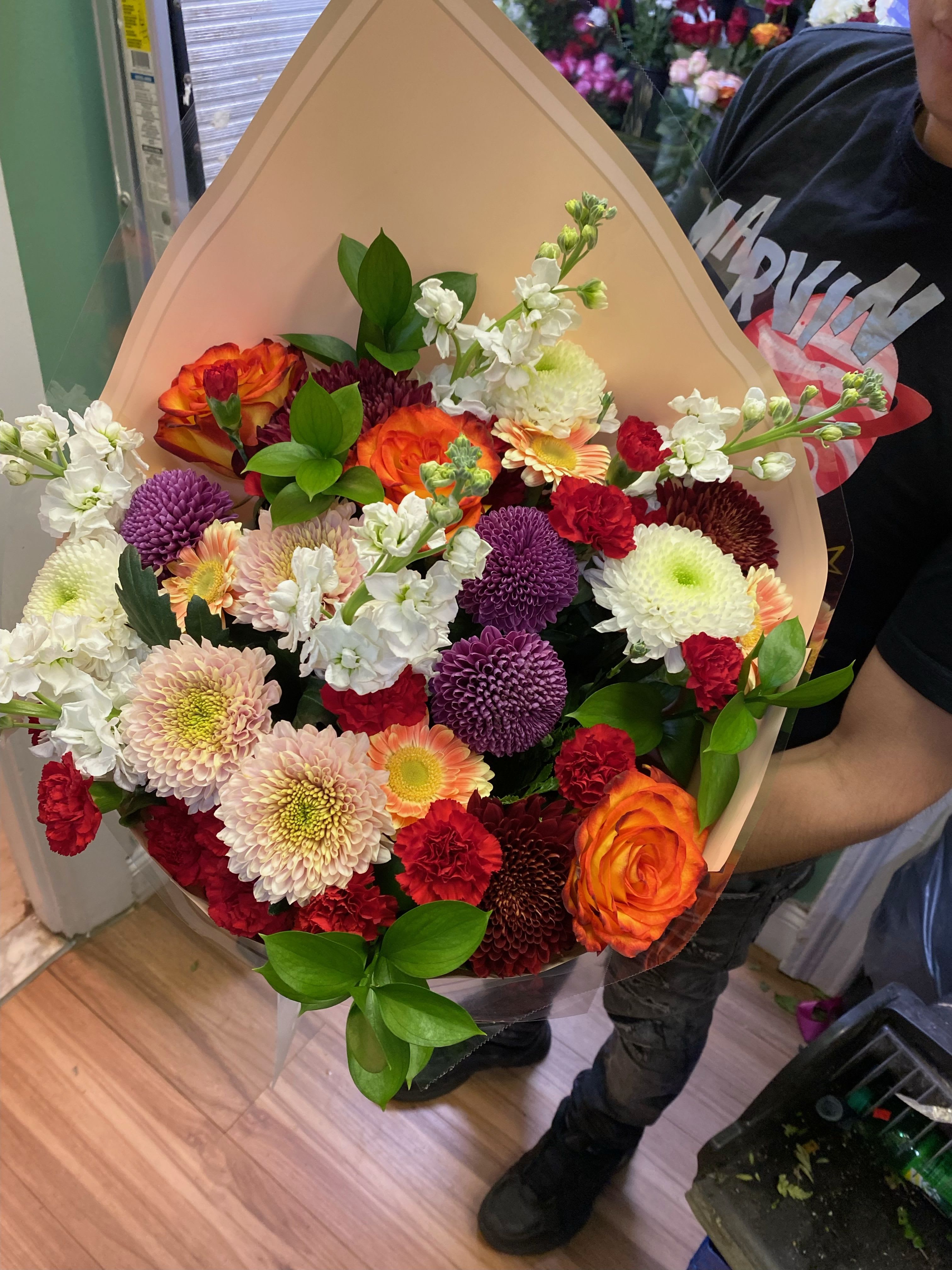 Everyday Bouquet - Bright, cheerful color and a full, rounded silhouette make this Everyday Bouquet the kind of mixed color flower arrangement that instantly lifts someone's spirits. Perfect as a birthday bouquet, a thank-you gift, or a just-because surprise, the combination of orange roses, white and purple chrysanthemums, red carnations and pale gerbera daisies creates an energetic, celebratory impression that will make the person you're thinking of feel genuinely seen.  This large arrangement pairs varied bloom sizes and textures-velvety roses, ruffled chrysanthemums, classic carnations and soft gerbera centers-for a lively contrast that reads fresh and abundant. The stems come wrapped in a peach-toned bouquet wrap with a clear plastic sleeve for protection, giving the bouquet a polished presentation while keeping blooms secure in transit.  Send this Everyday Bouquet when you want to brighten someone's day, mark a small victory, or say thank you with color and warmth; it's designed to arrive ready to display and delight. For best results, trim stems and change the water daily to keep the mixed flowers looking their freshest.