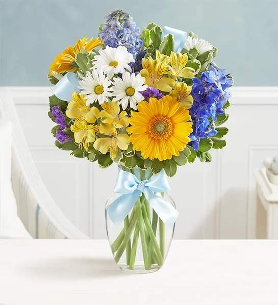 Mixed bouquet of daisies, gerberas, and blue flowers in a glass vase