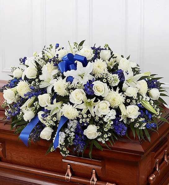 White and blue floral spray arranged on a wooden casket