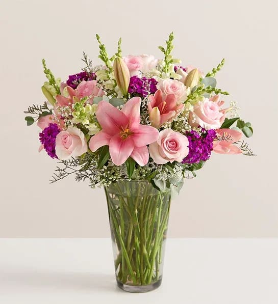 Pink lilies and roses arranged in a clear glass vase
