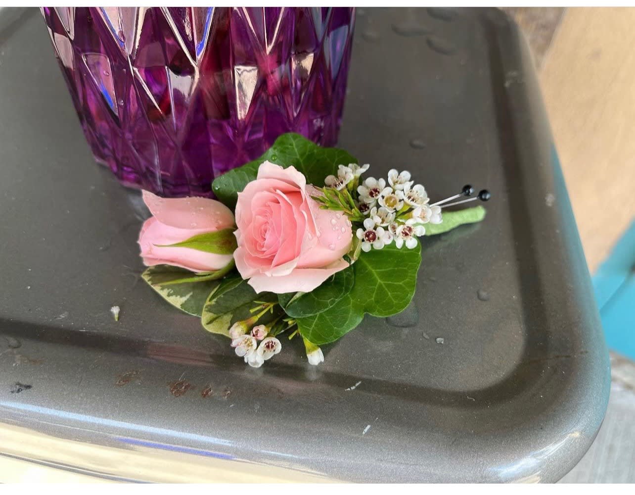 Pink rose boutonniere with small white blossoms and pins on a gray surface
