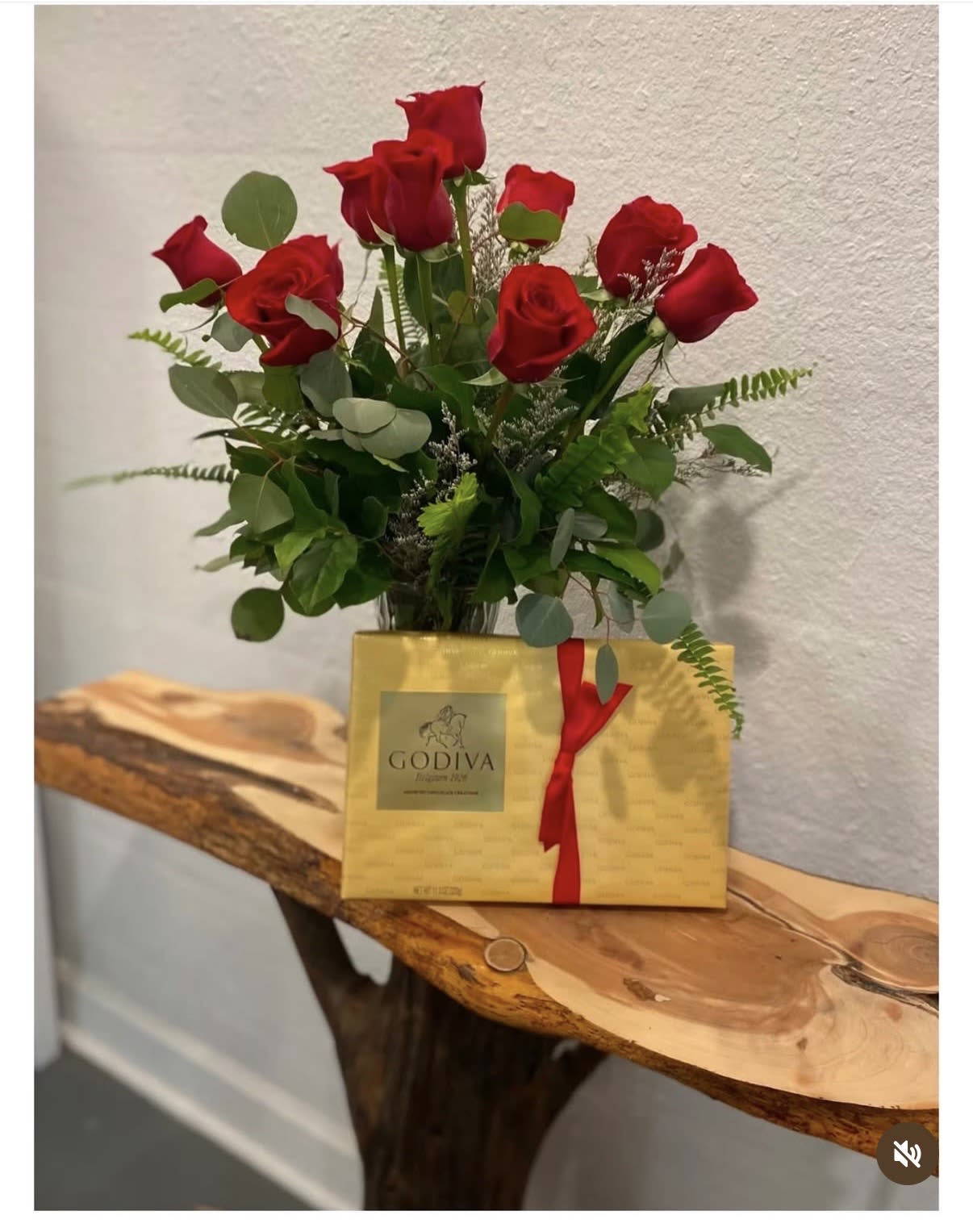 Red roses arranged in a vase with a gold Godiva gift box