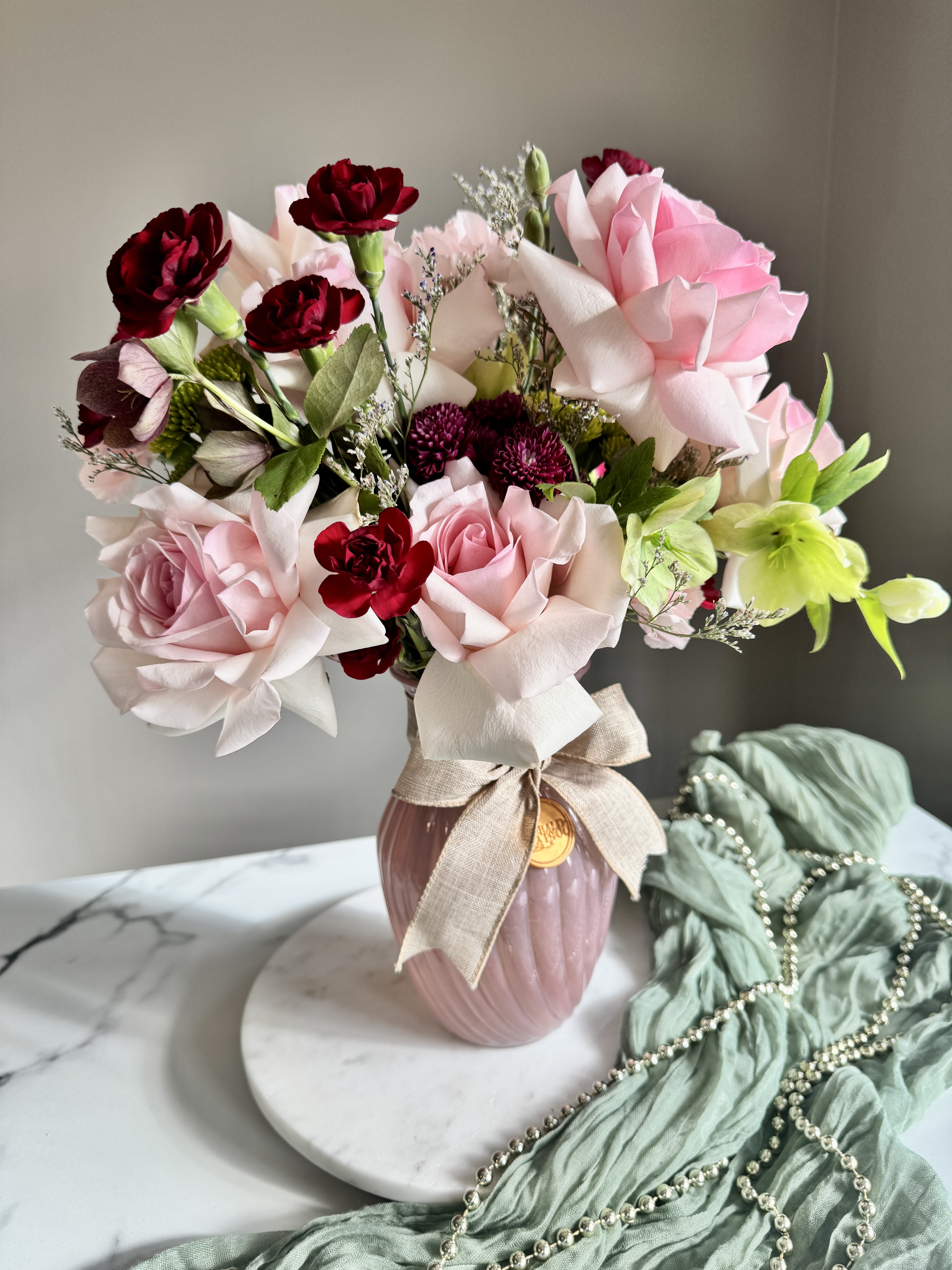 Pink and burgundy roses arranged in a vase with a ribbon bow