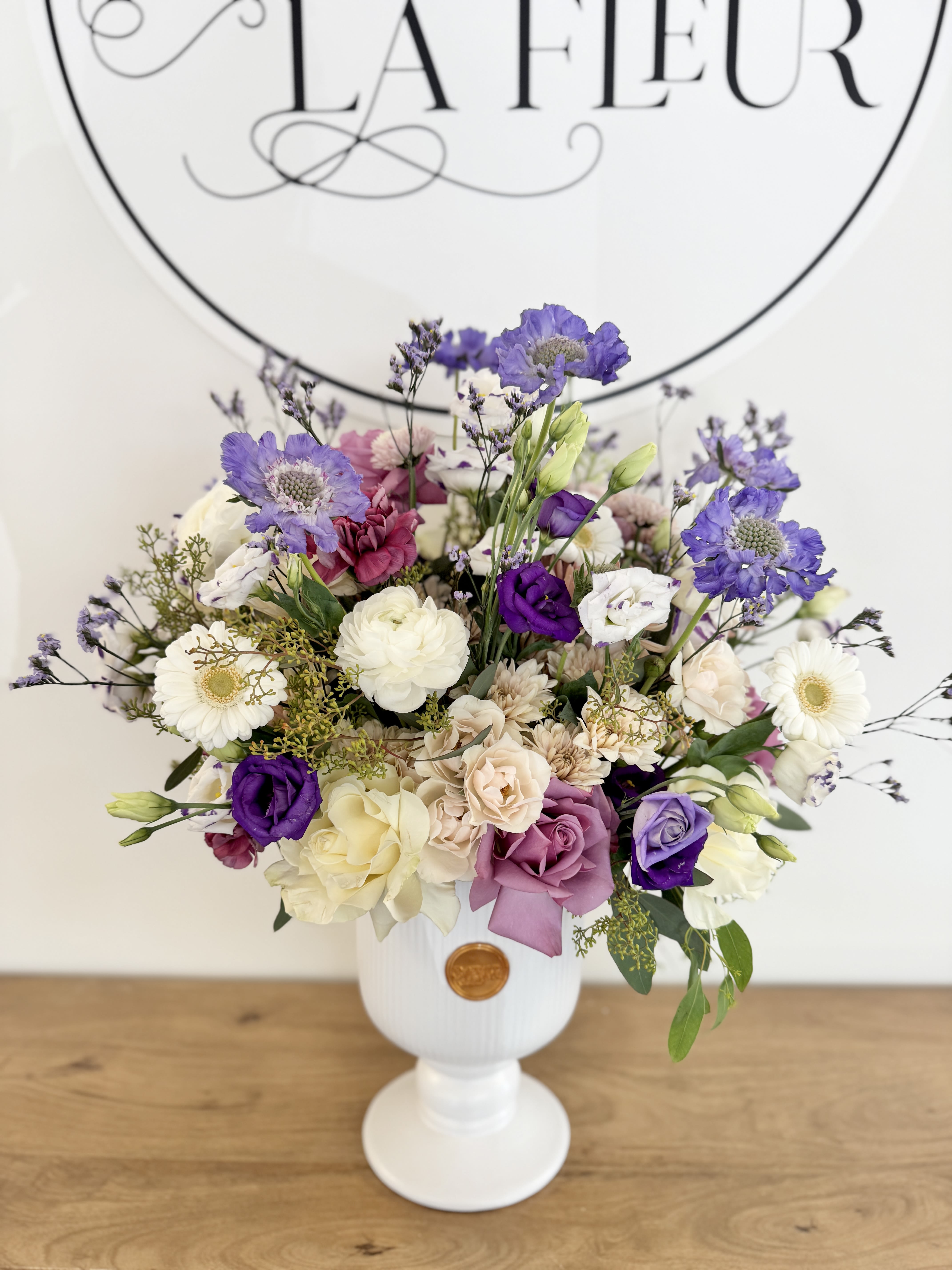 Whispered Garden - Delicate yet striking, the Whispered Garden features a luxurious selection of premium seasonal flowers artfully curated by the florist and arranged in a timeless white ceramic urn. Designed with graceful movement, airy textures, and a naturally gathered aesthetic, each arrangement is one of a kind, showcasing the freshest blooms of the season. An elegant statement piece for celebrations, heartfelt gifts, or bringing refined beauty into any space. 