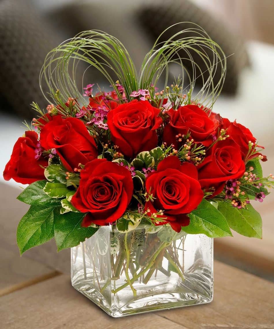 Red roses arranged in a clear square glass vase with decorative loops