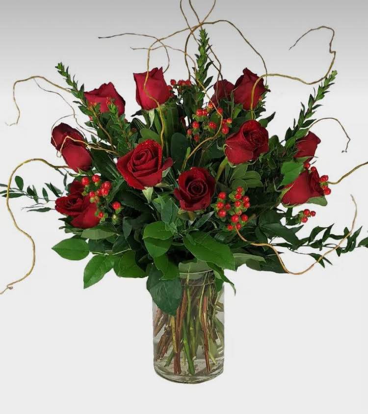 Red roses arranged in a clear glass vase with greenery and berry accents