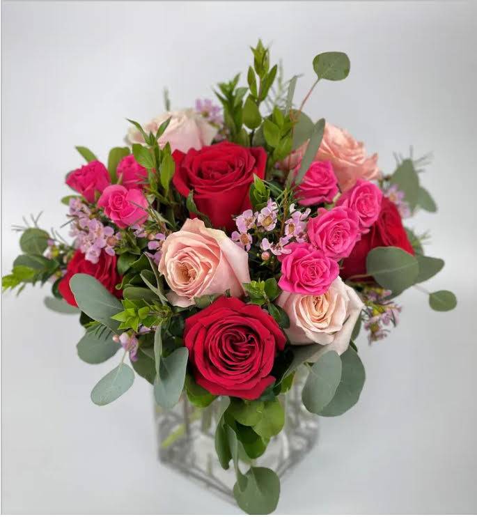 Bouquet of red, pink, and blush roses in a clear glass vase