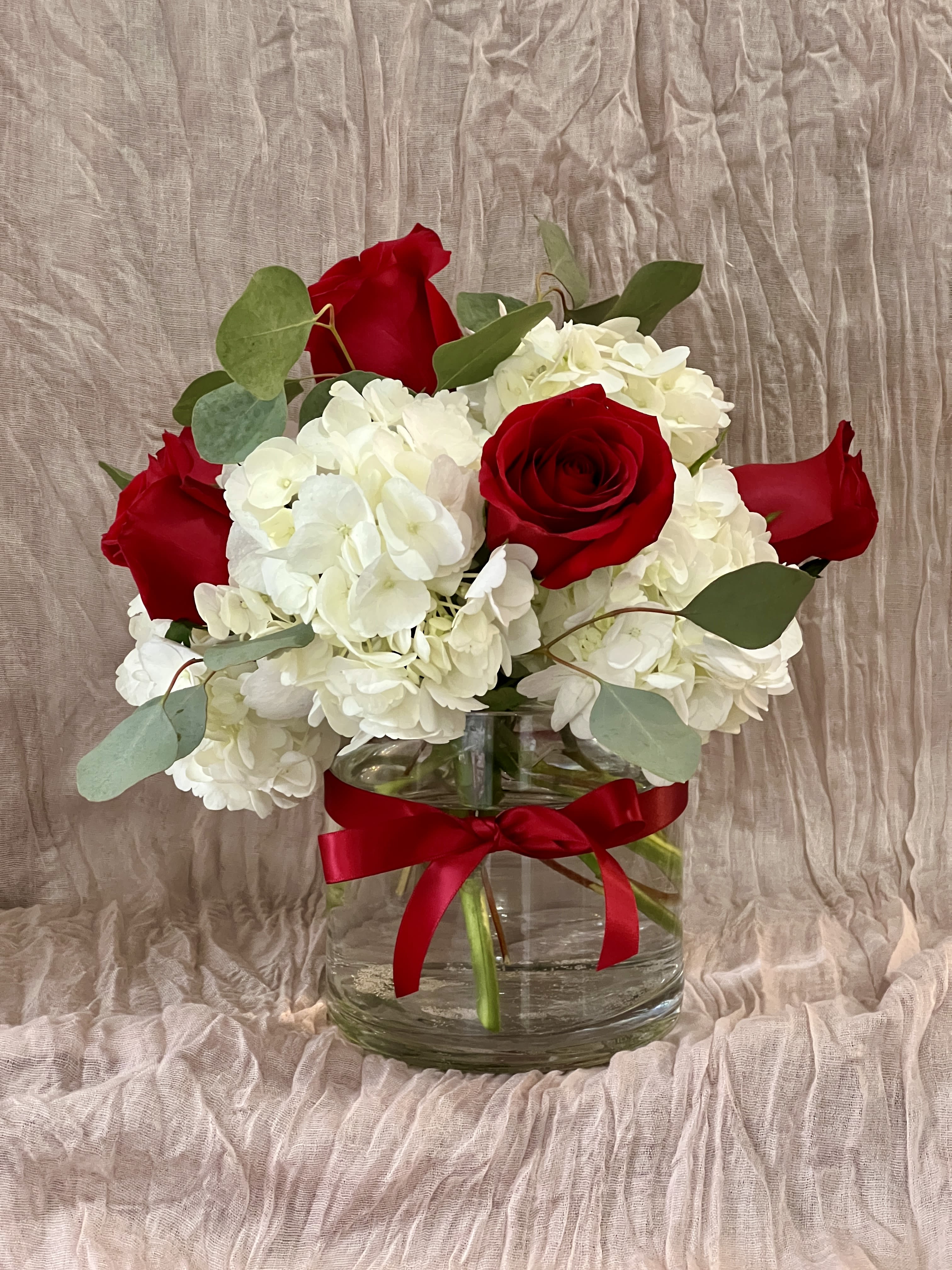Red roses and white hydrangeas in a clear glass vase with a red ribbon