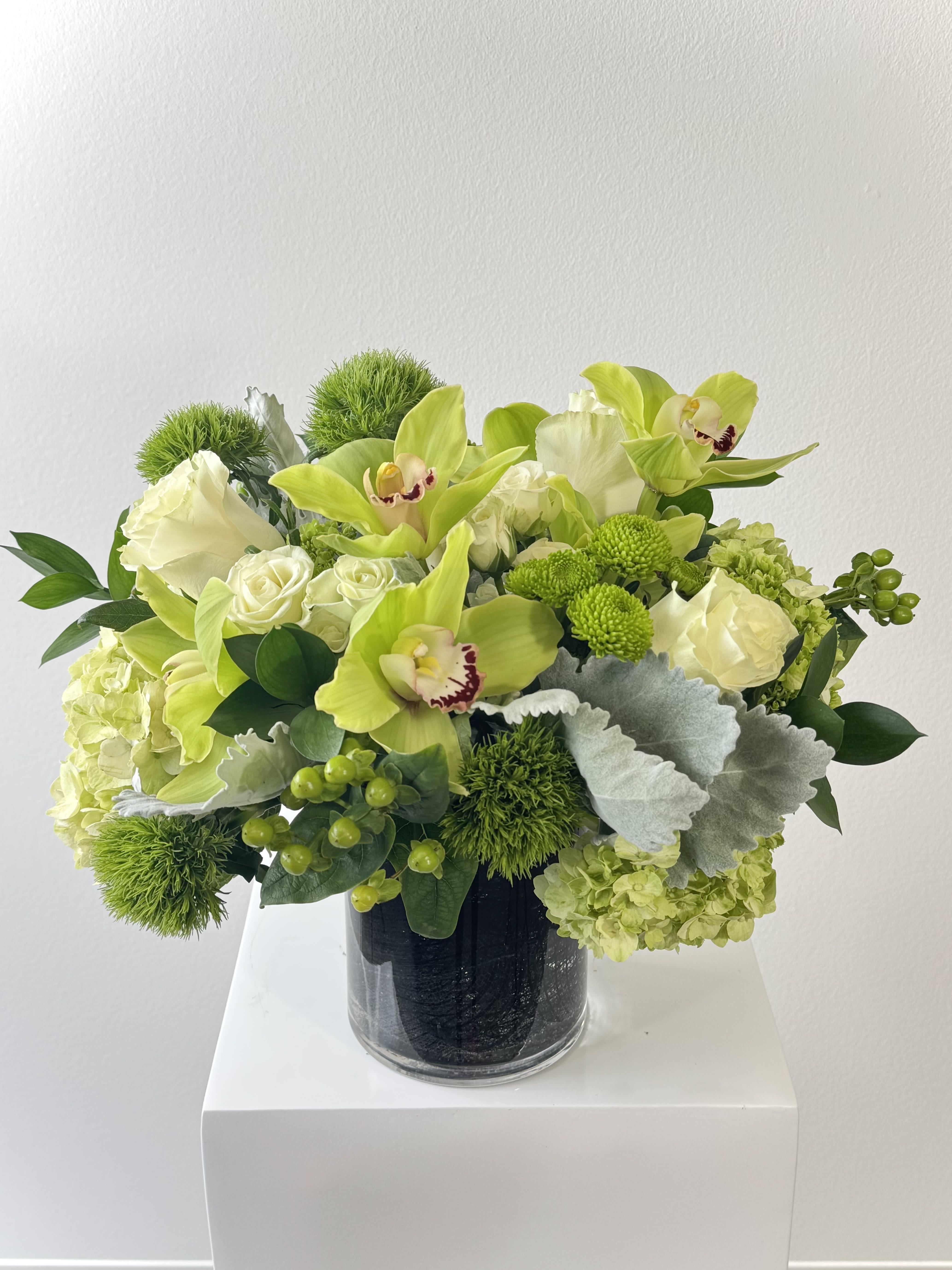 Green and white floral arrangement in a glass vase