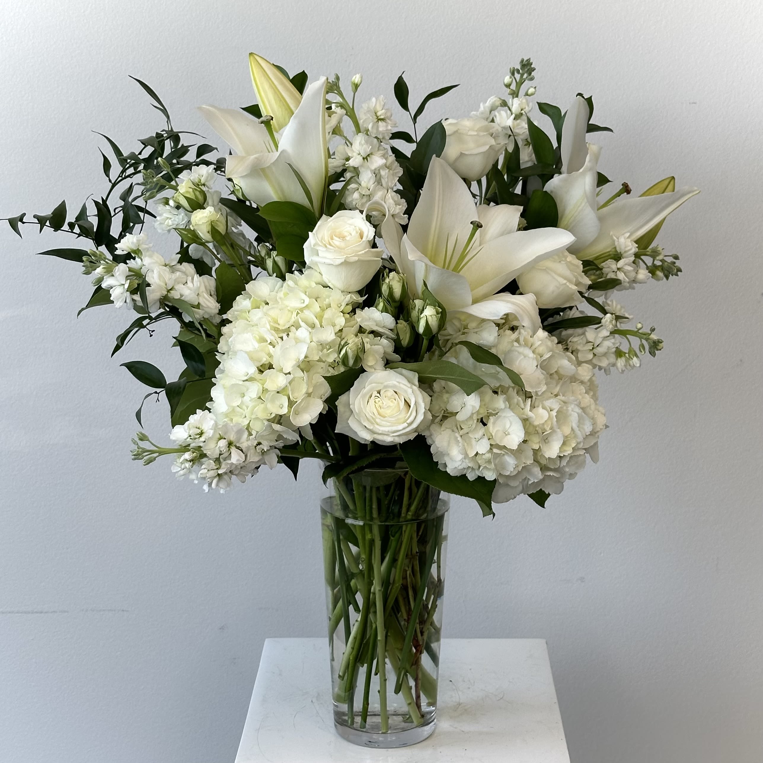 Dreams From the Heart - A tender embrace of calm and comfort awaits at IrvineVillageFlowers.com. Perfect for those seeking solace, this lovely bouquet gathers white and cream blossoms into a gentle gift that whispers hope and strength. Nestled in a tall glass vase, it’s a soothing presence for any heart in need.    White hydrangeas bloom with quiet grace, their soft petals symbolizing love and understanding, offering a lasting sense of peace. Spray roses in pure white weave in delicate beauty, their presence a reminder of purity and resilience. Cream roses glow with warmth and affection, wrapping the arrangement in a comforting hug. Accented by the silvery softness of eucalyptus and the subtle charm of stock, this bouquet—oriented one-sided for standard, or all-around for deluxe—brings a serene unity that eases the soul. Each flower works together to create a meaningful gesture, perfect for sharing care and compassion with someone dear.    Find this tranquil treasure at Irvine Village Flowers. Visit us online or in-store, and let our reliable flower delivery across Irvine bring this comforting bouquet straight to your loved one, fresh and ready to soothe. A gentle bloom of hope, crafted with love.