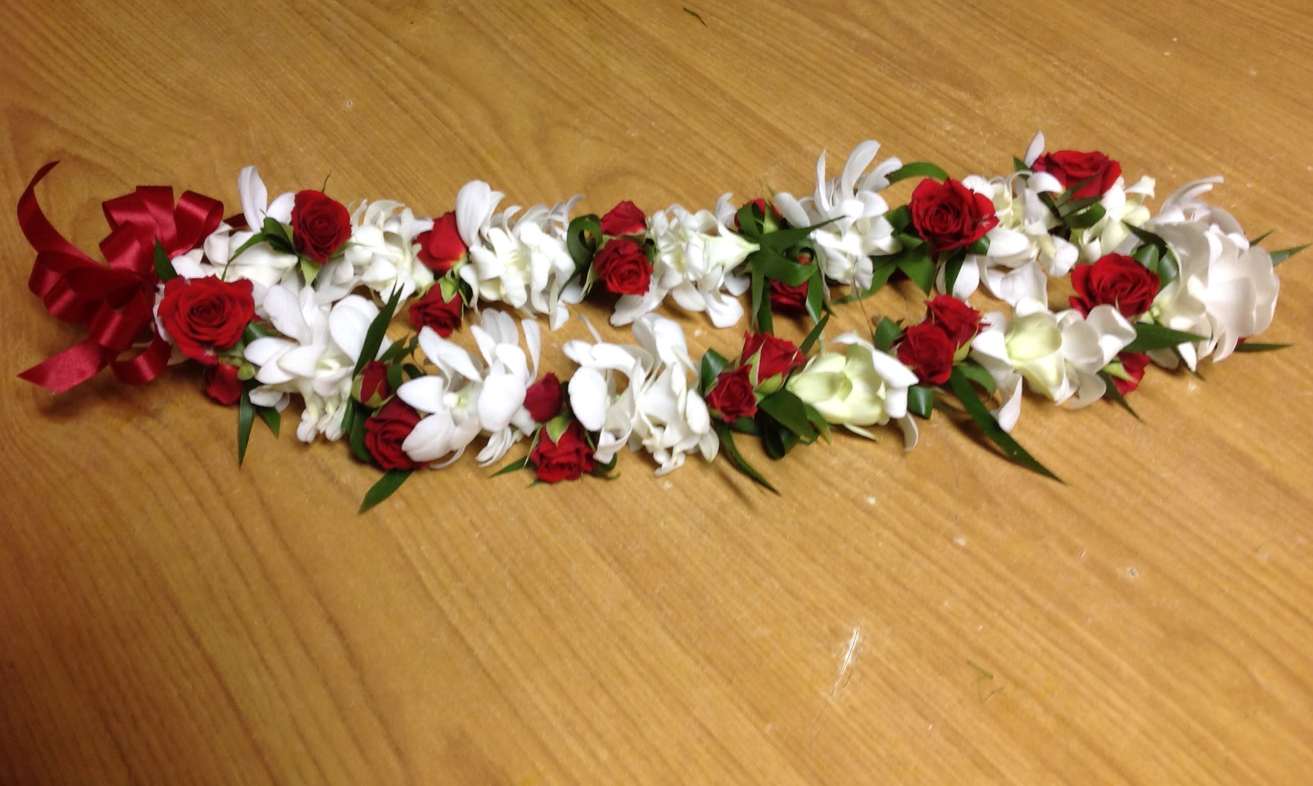 Red and white floral lei with ribbon on a wooden surface