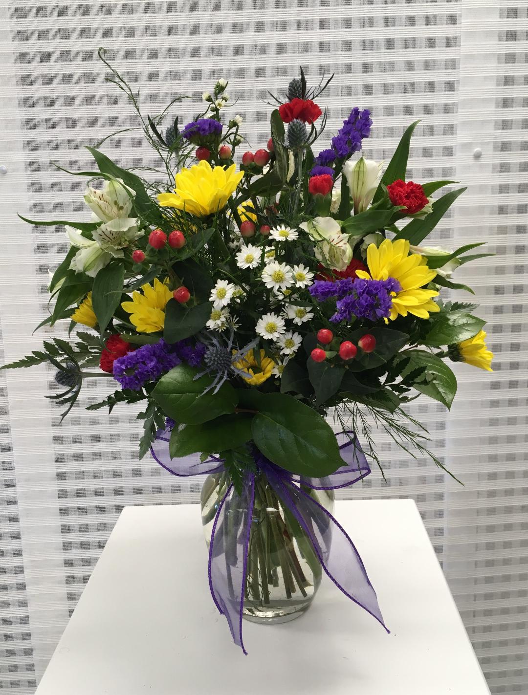 Mixed bouquet in a clear glass vase with yellow, purple, red, and white flowers