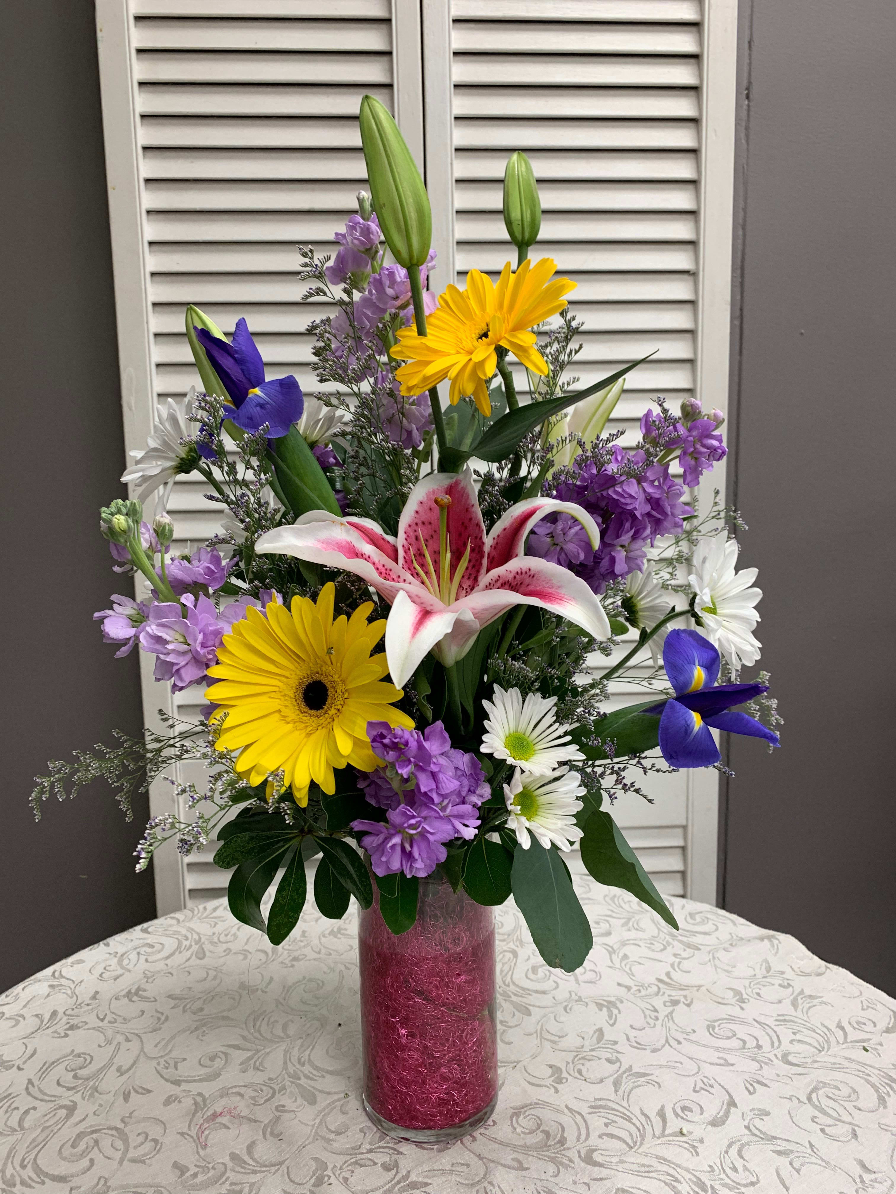 Mixed bouquet of lilies, daisies, and purple flowers in a tall glass vase