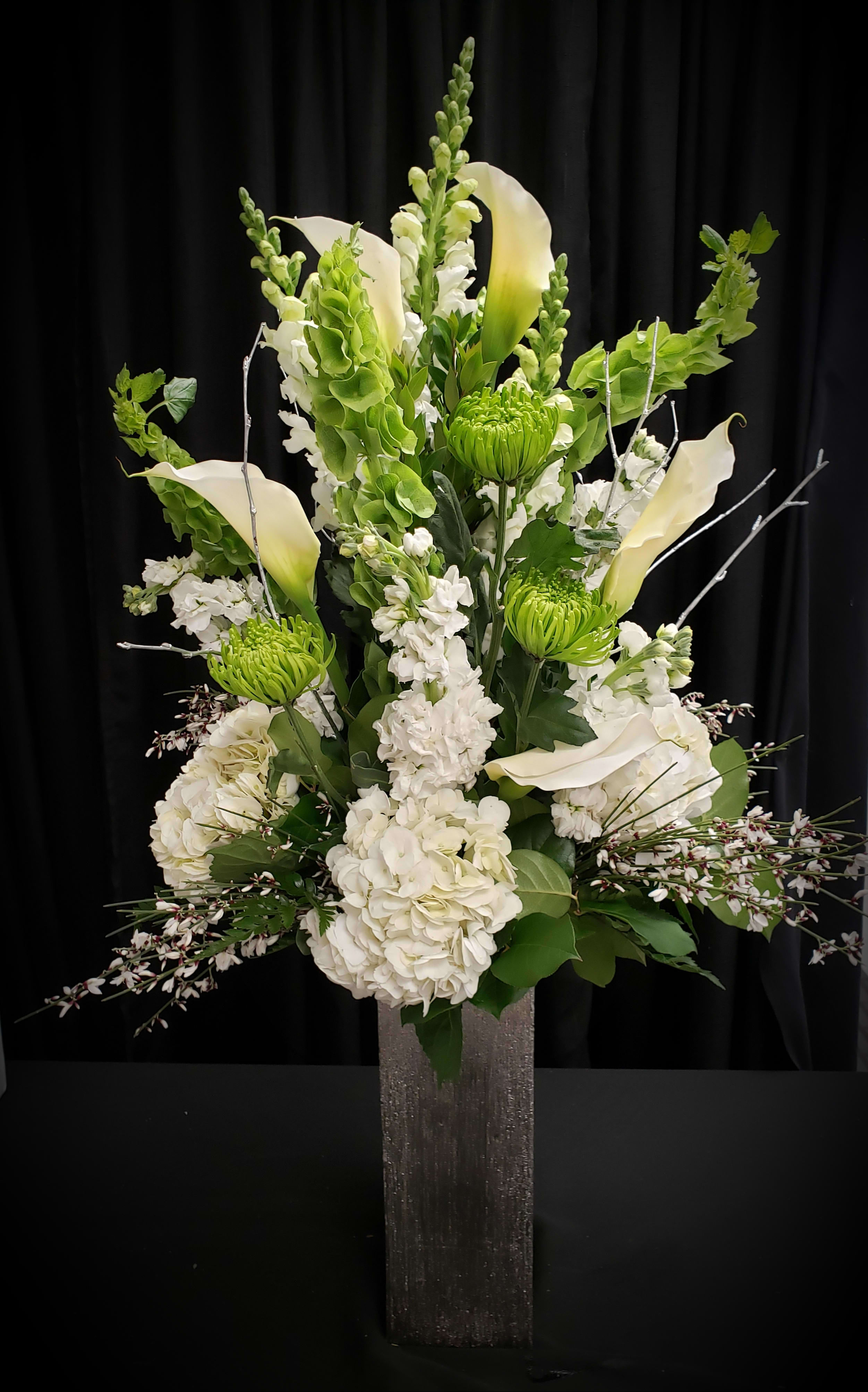 Tall white floral arrangement with calla lilies and green blooms in a square vase