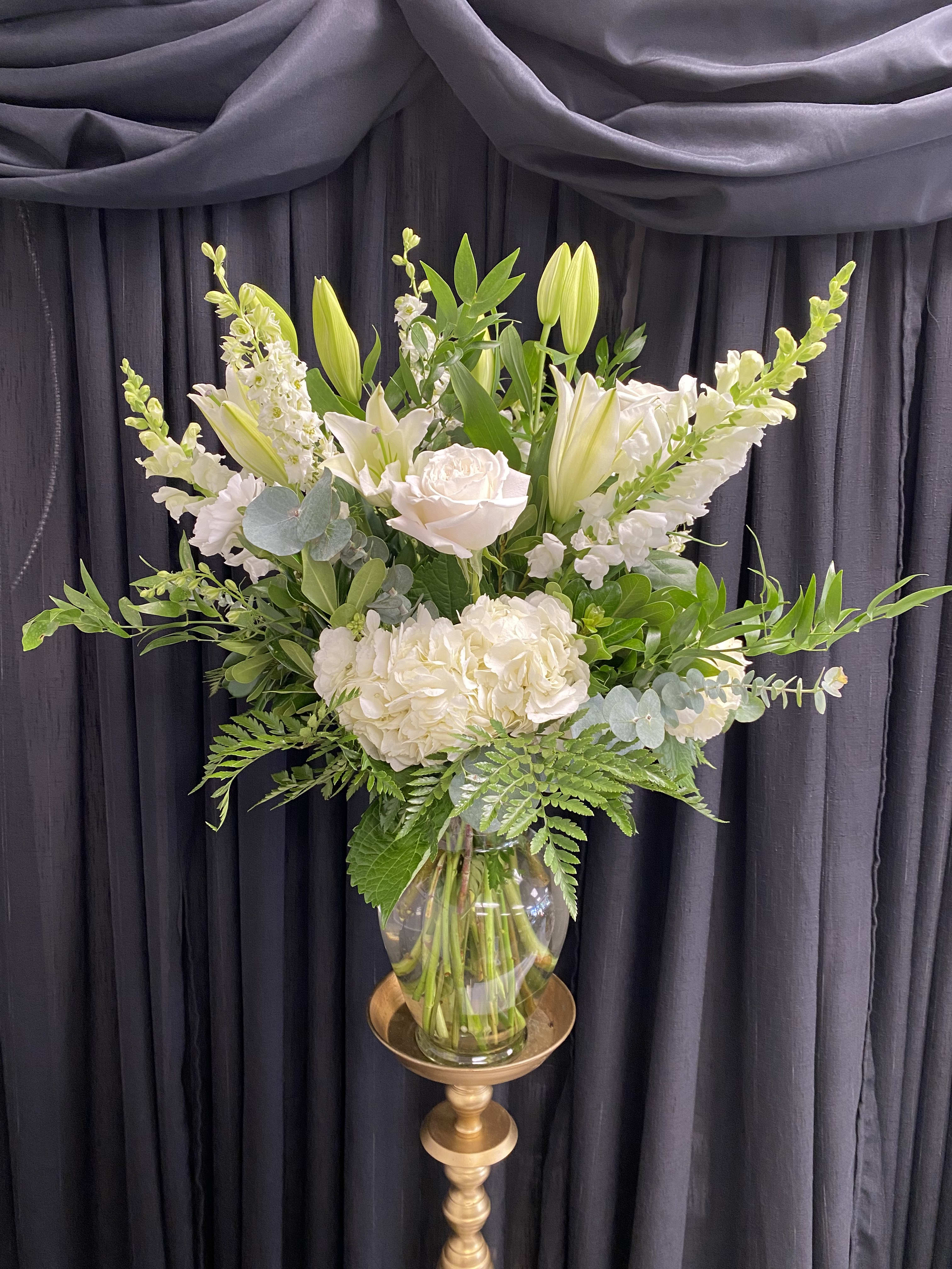 White floral arrangement in a glass vase on a gold pedestal stand