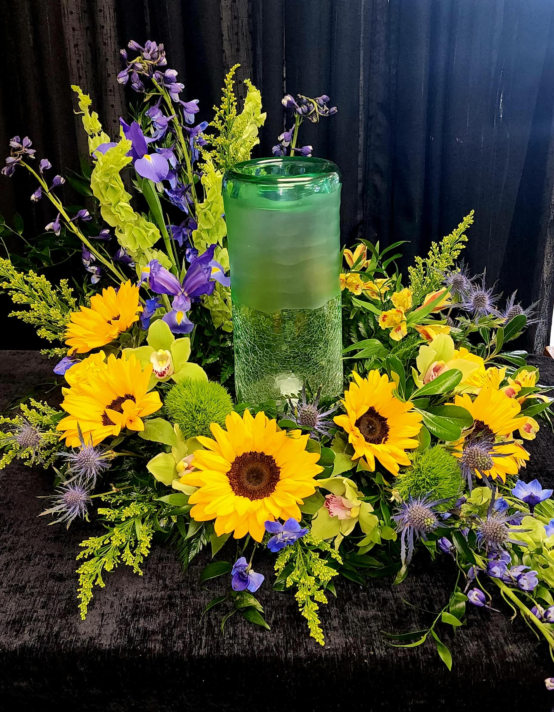 Yellow sunflowers and purple flowers arranged around a green glass candle holder