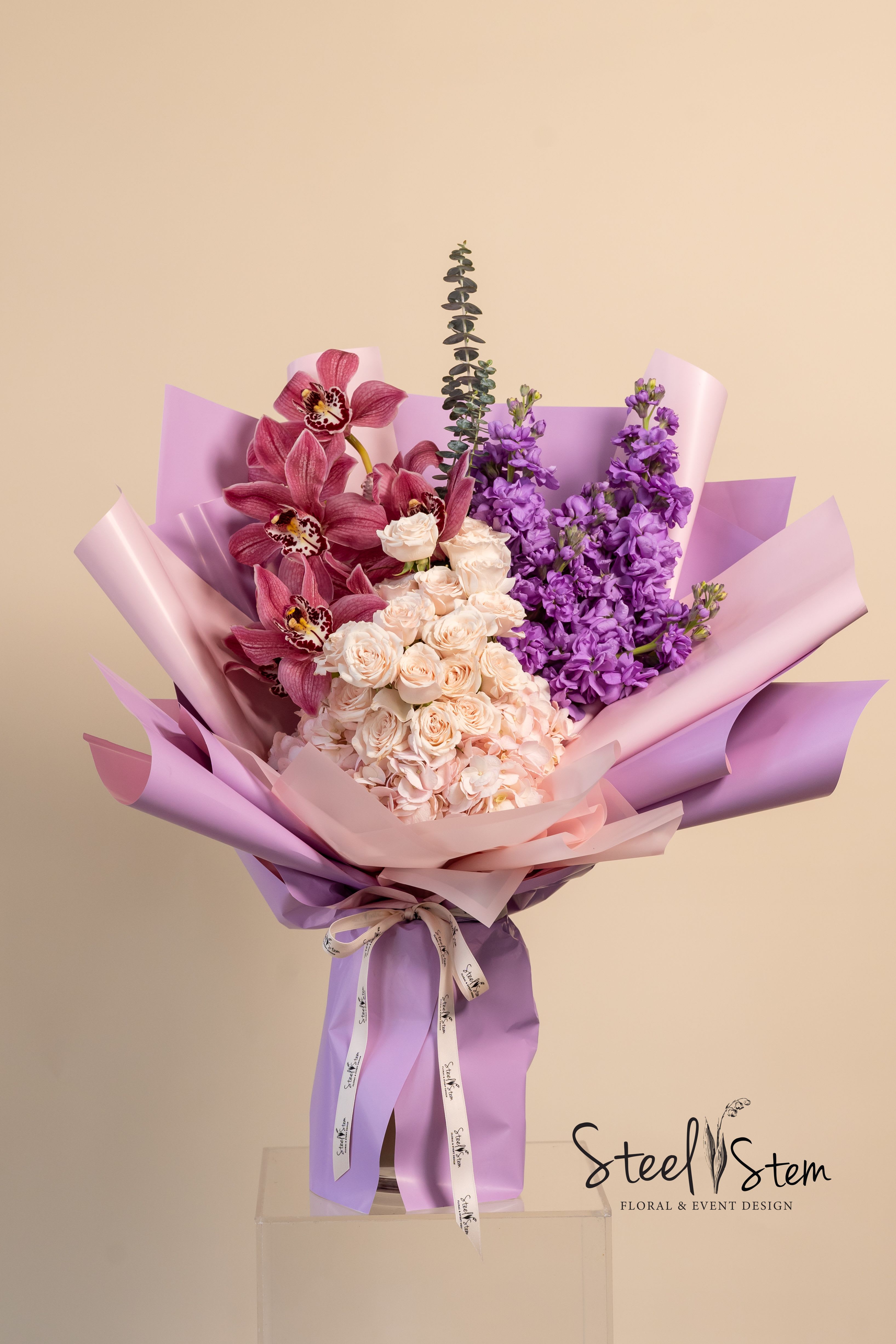Bouquet of pink orchids, roses, and purple flowers wrapped in lavender paper