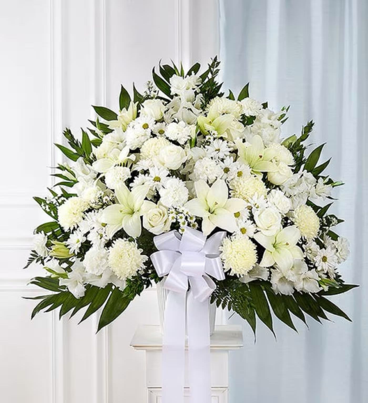White floral spray with lilies and chrysanthemums in a vase, tied with a white ribbon