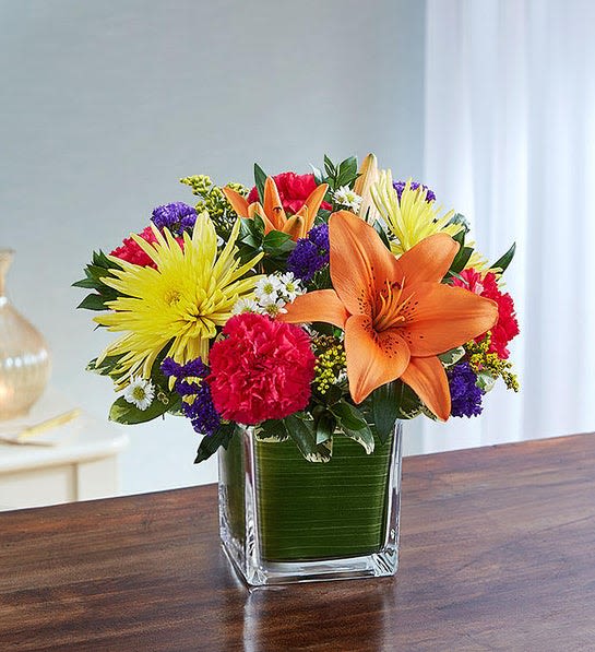 Colorful bouquet with orange lilies, yellow daisies, and pink carnations in a glass vase