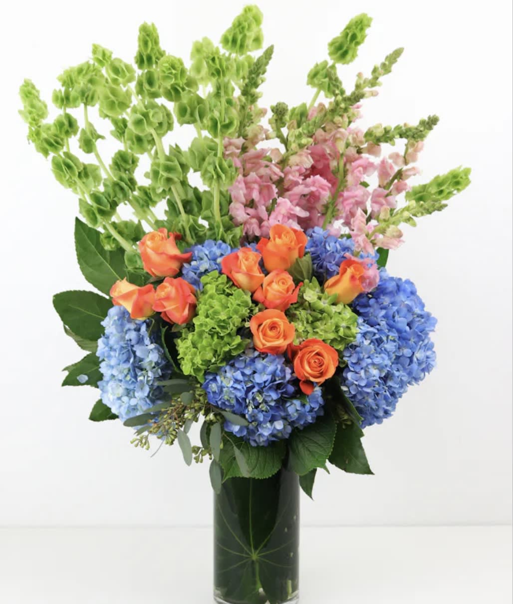 Bouquet of blue hydrangeas, orange roses, and pink snapdragons in a glass vase