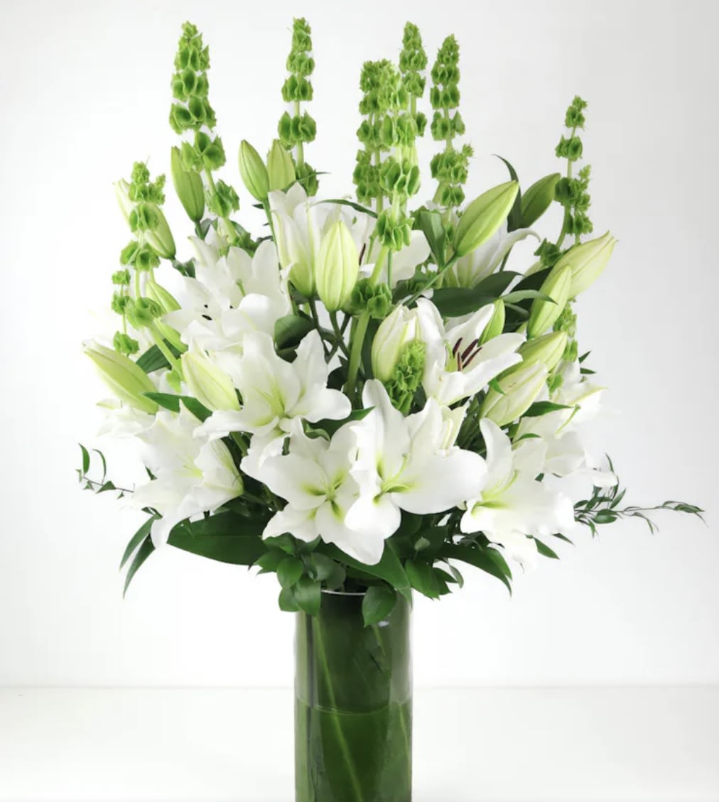 White lilies and green spikes arranged in a tall glass vase