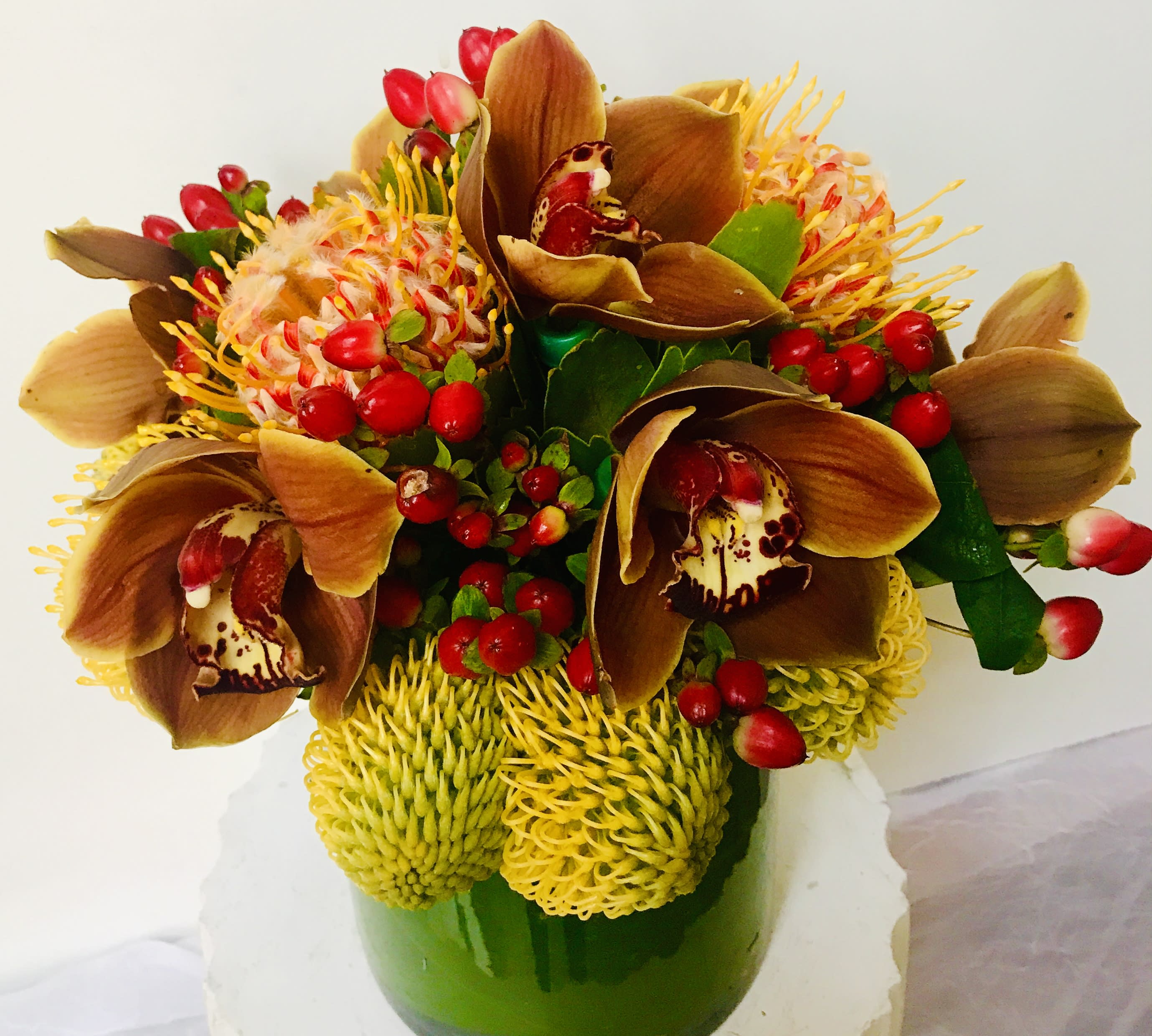 Bouquet with brown orchids, yellow pincushion blooms, and red berries in a green vase
