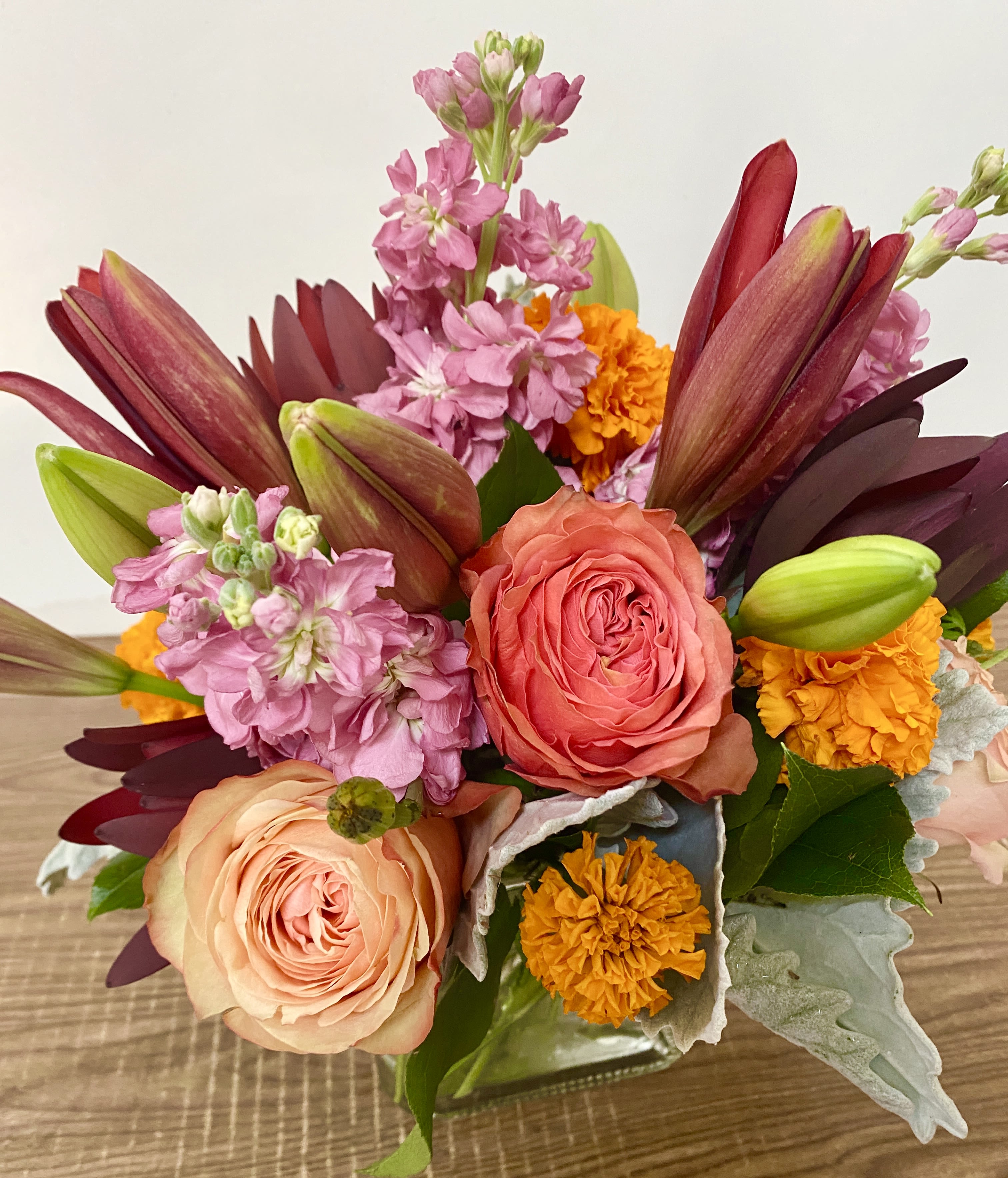 A SOLO  MIO - In the clear glass, square vase combinations or orange flowers lilies, marigold, pinch  roses and greenery 