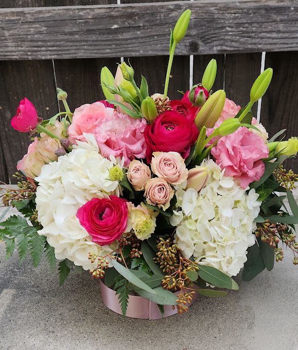 Low pink hatbox arrangement with white hydrangeas, pink spray roses, ranunculus, and lily buds