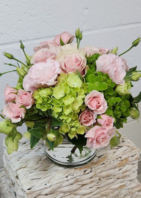 Round arrangement of pale pink roses and green hydrangeas in a clear glass vase