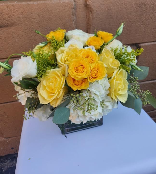 Low arrangement of yellow and white roses with white hydrangeas in a clear glass cube vase