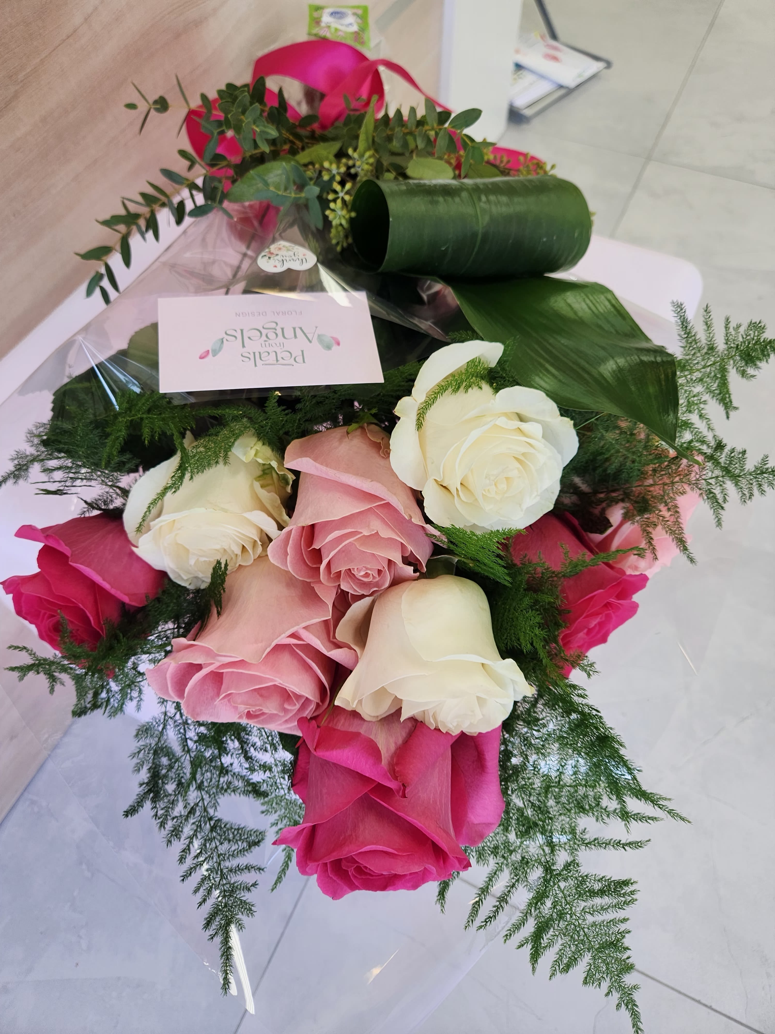 Hand-tied bouquet of pink and white roses with decorative greenery in clear wrap and a pink ribbon