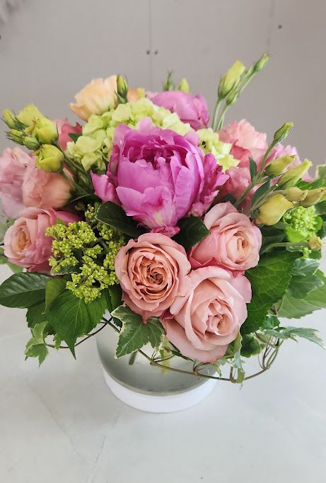 Low round arrangement of pink peonies and roses with green hydrangea in a white bowl vase