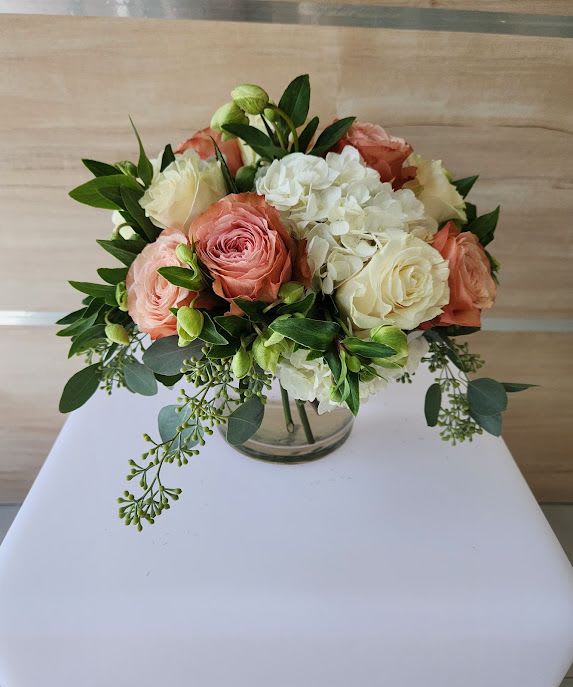 Short round bouquet of peach and cream roses with white hydrangeas in a clear glass vase