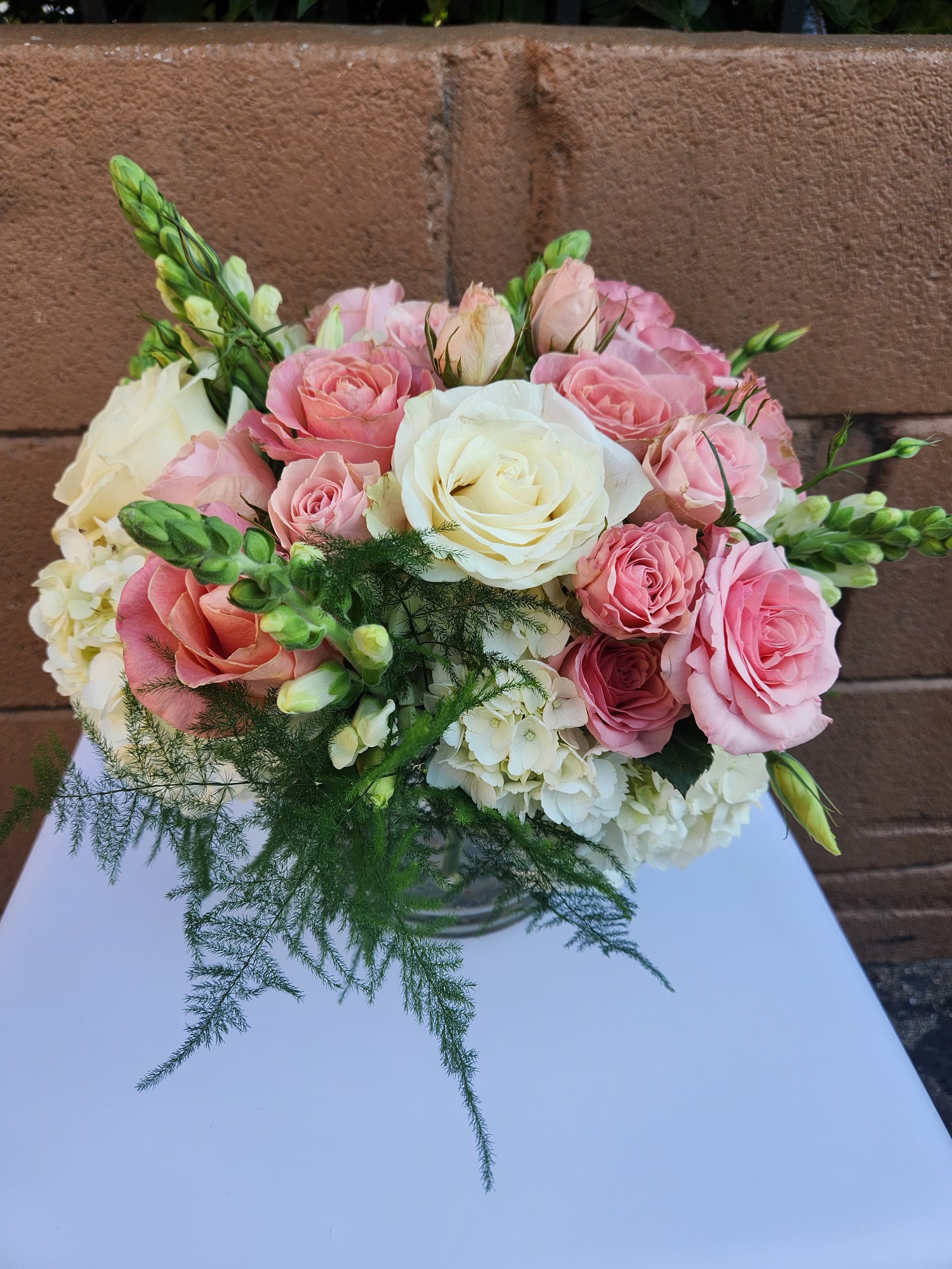 Round arrangement of pink and white roses with hydrangeas in a clear glass vase