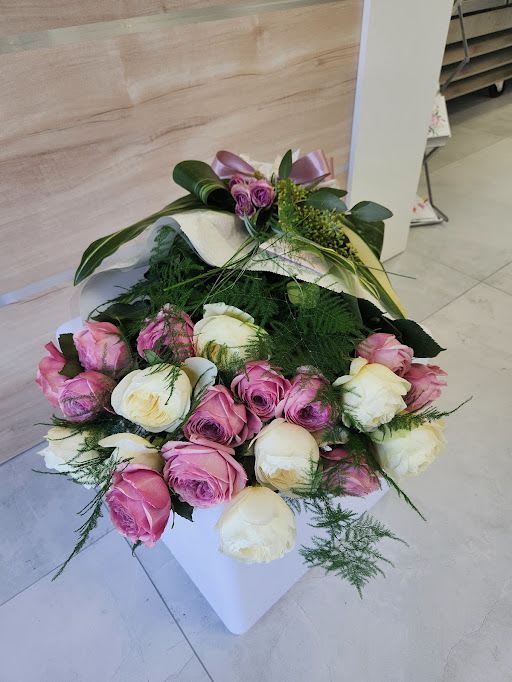Low arrangement of pink and cream roses in a white square container with a decorative bow.