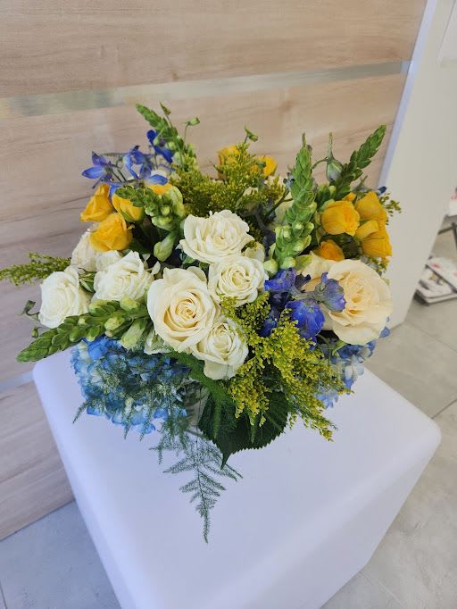 Round arrangement of cream roses, yellow blooms and blue flowers in a compact mixed bouquet