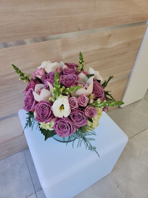 Low round arrangement of lavender roses with white blooms in a clear glass bowl vase